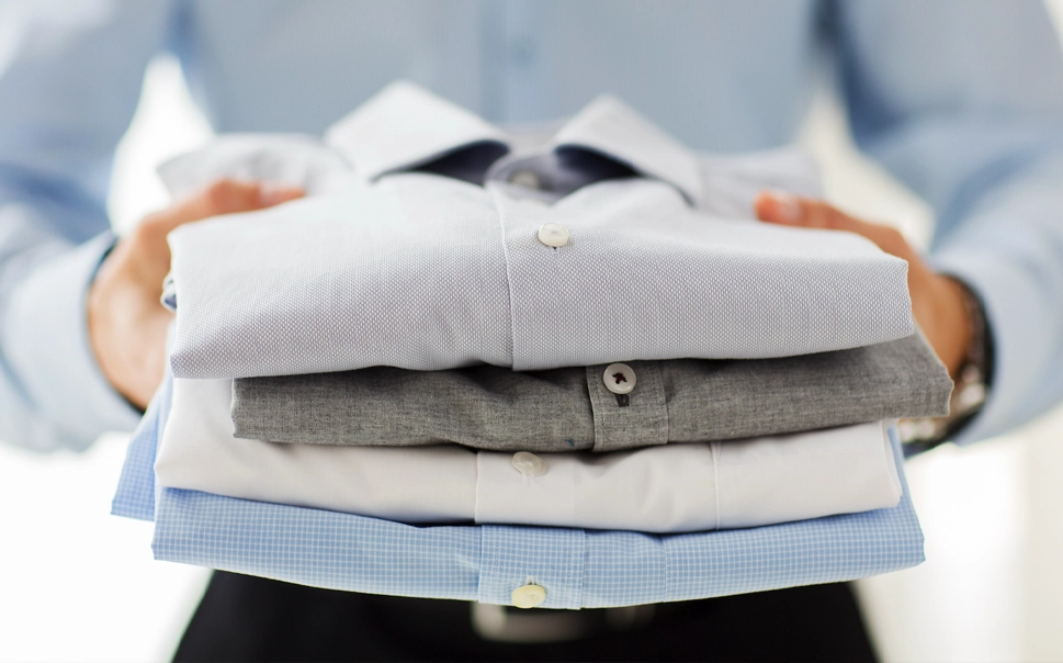Person holding a neatly folded stack of four collared shirts in different colors and patterns.