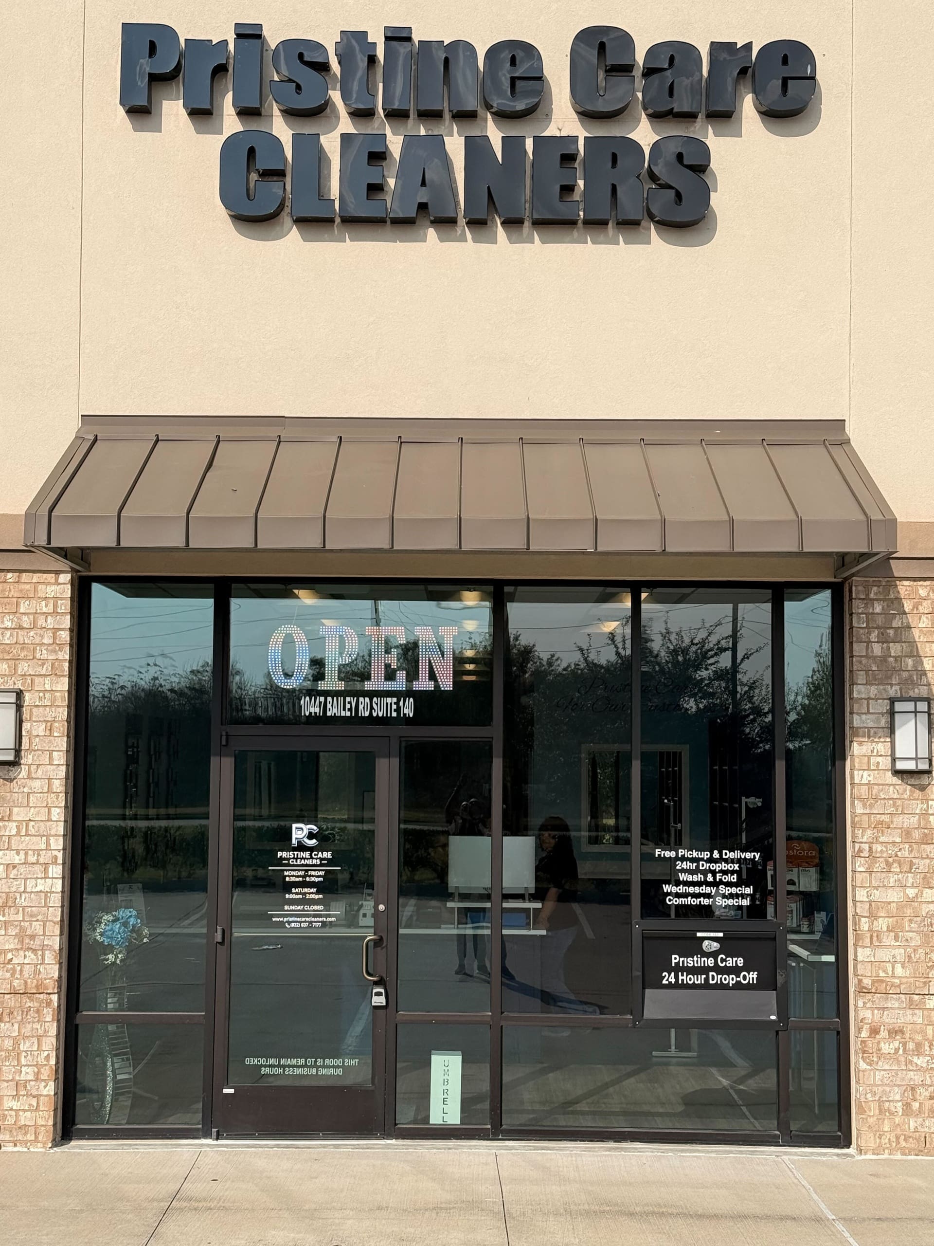 Storefront of Pristine Care Cleaners with large sign, glass doors, visible “OPEN” sign, and business hours listed on the door.