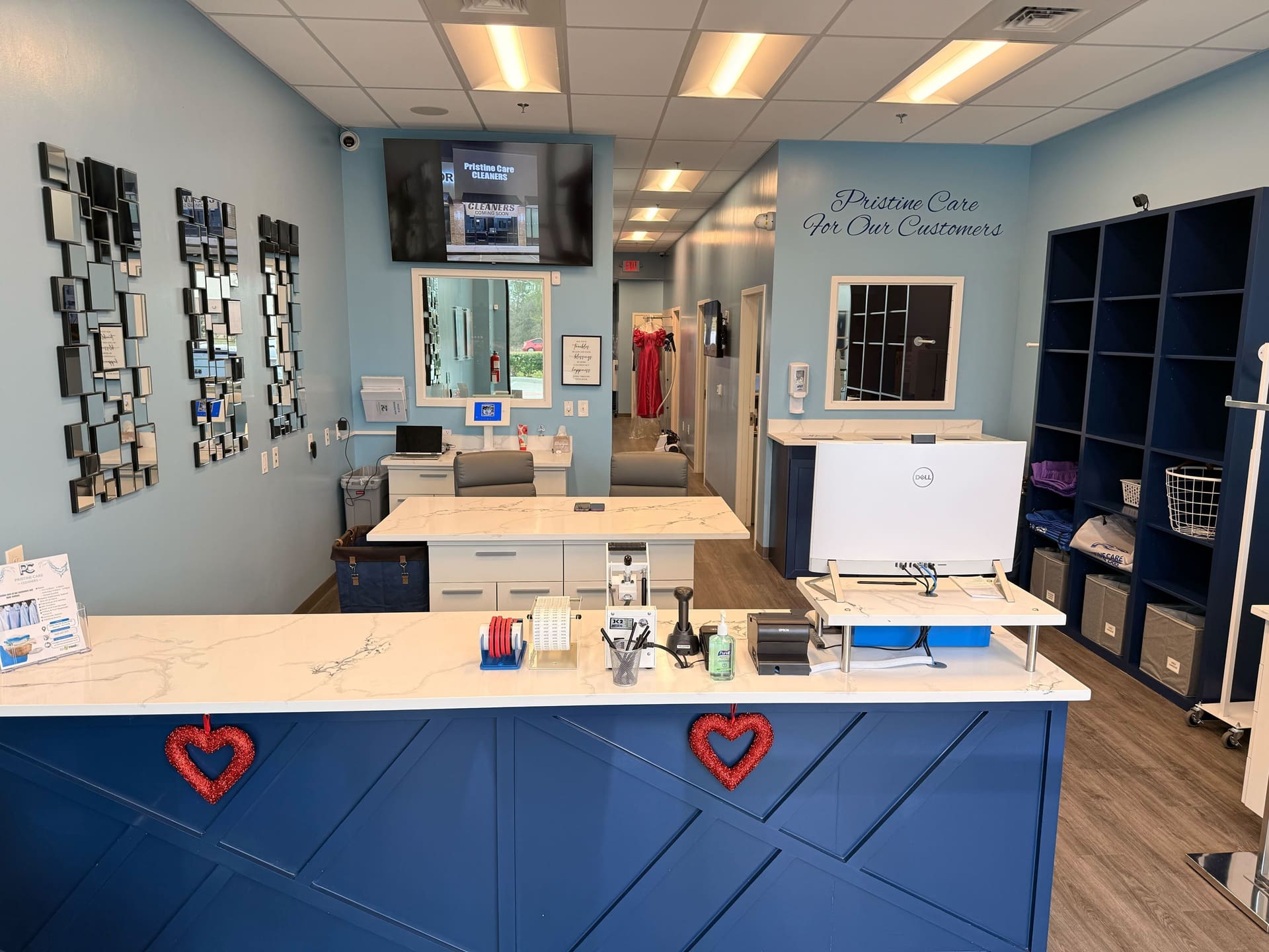 Modern dry cleaning shop with a marble counter, computers, mirror decor, blue walls, baskets, and cleaning items, with a sign reading 